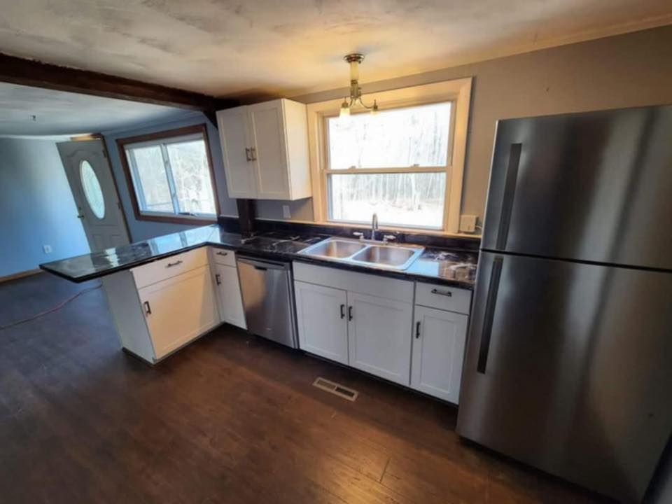 Small kitchen with white cabinets, black countertops, stainless fridge, and window over the sink