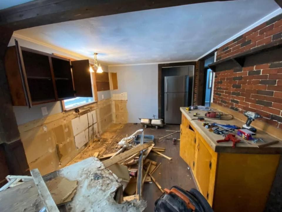 Partially demolished kitchen with debris, exposed brick wall, and yellow cabinets in a narrow room
