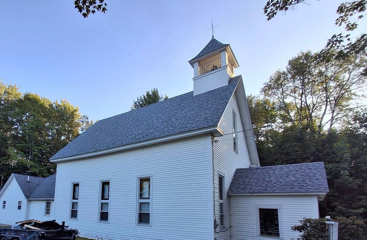 White wooden church with steeple and arched windows among trees on a sunny day