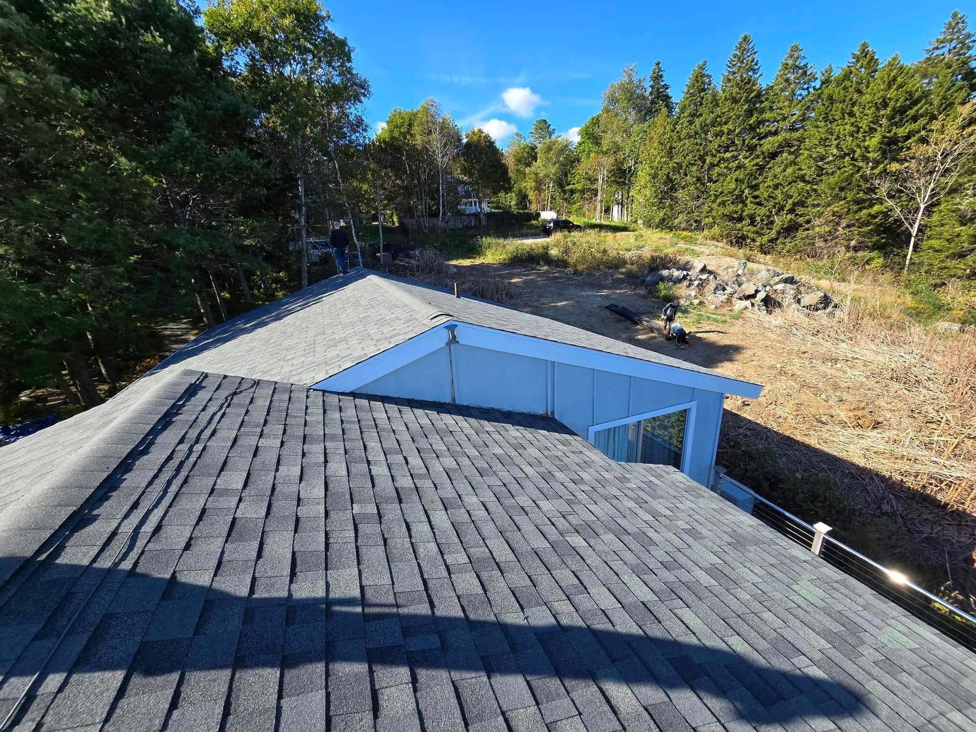 Blue-roofed building viewed from above, surrounded by trees and a rocky clearing under clear skies