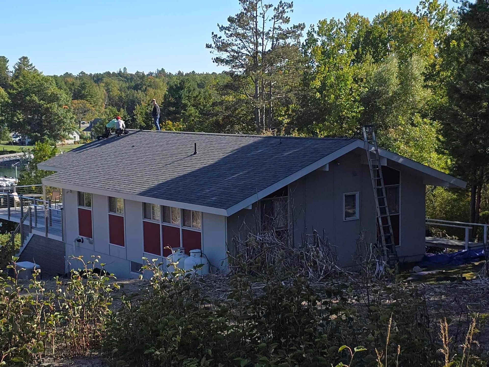 Small gray house with a dark roof in a wooded neighborhood, seen from above.