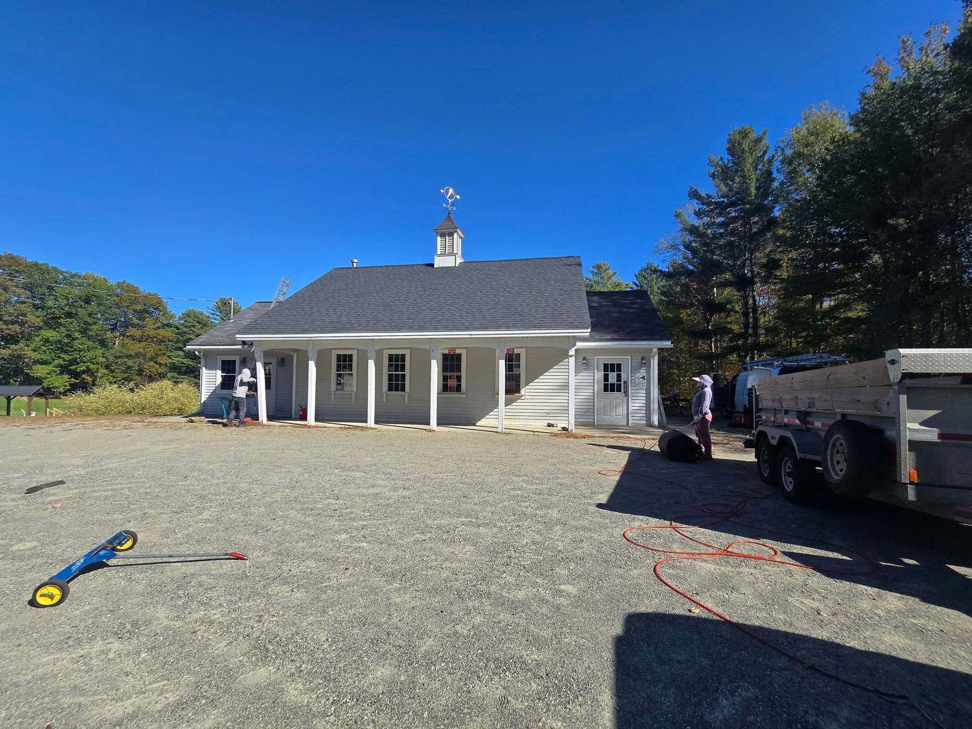 Small white house with porch and gravel driveway, truck parked beside it under a clear blue sky