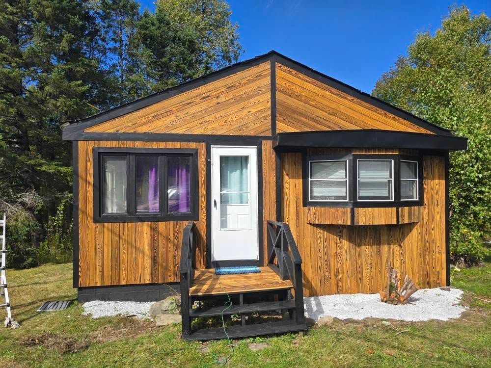 Small wooden cabin with a white door and black porch steps under a blue sky