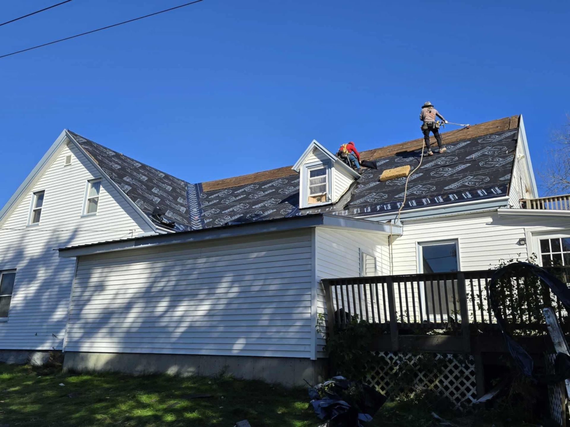 Two workers repairing a white house roof under a clear blue sky