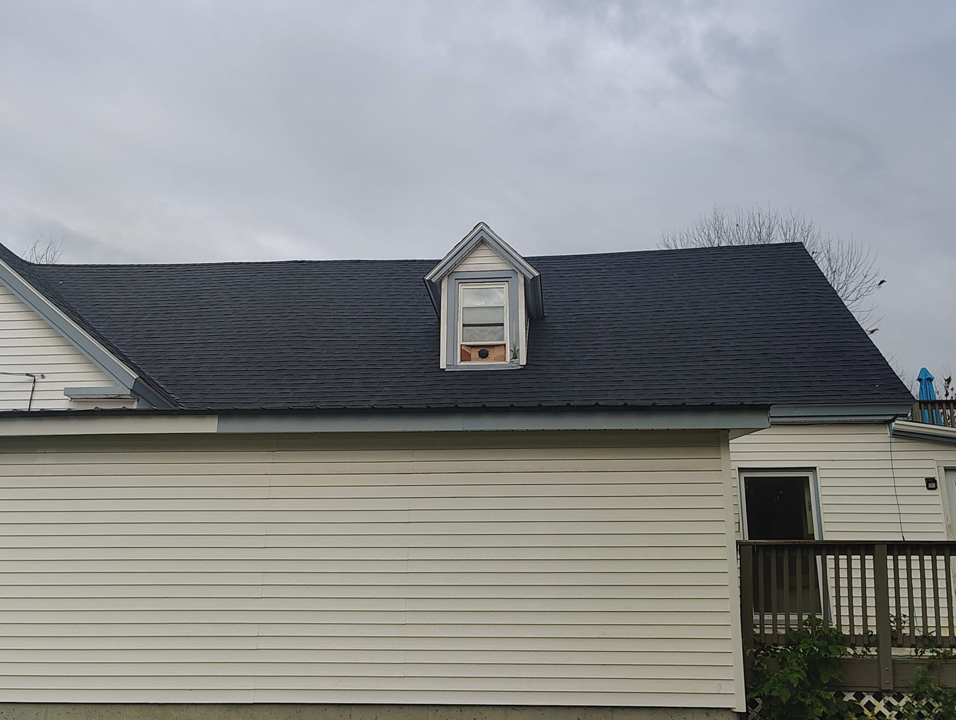 White house exterior with dark shingled roof and small dormer under a cloudy sky