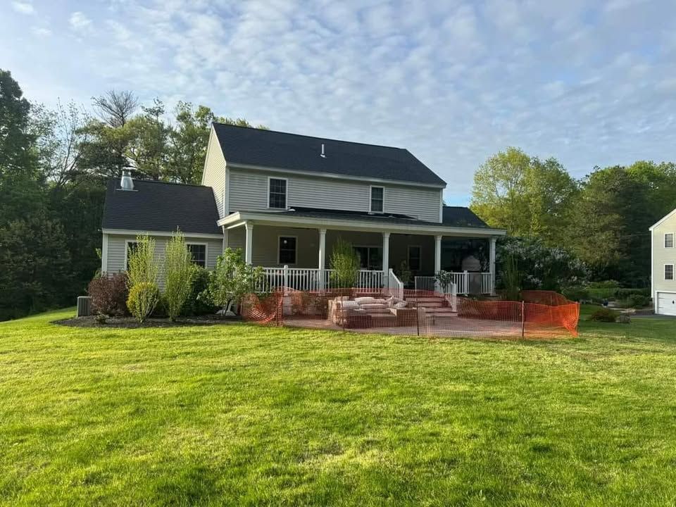 Two-story house with a porch and orange safety fencing in a grassy yard under a blue sky