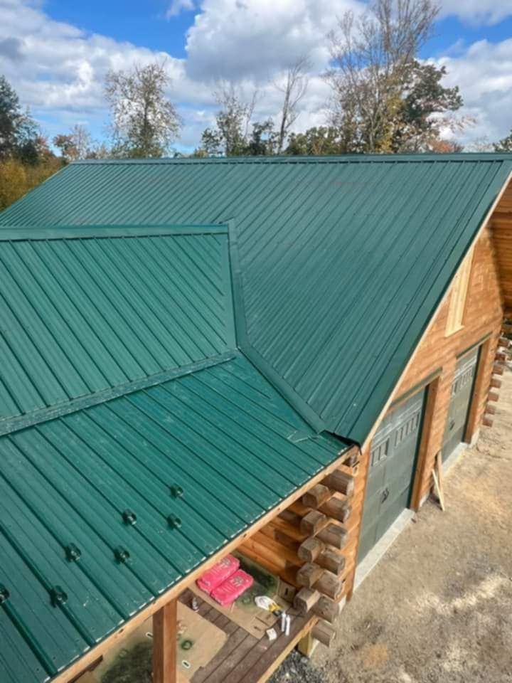 Green metal roof on a wooden house viewed from above, with trees and blue sky in the background