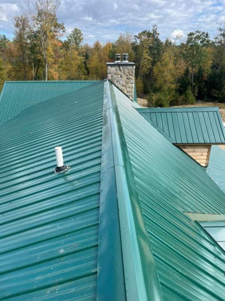 Green metal roof with a stone chimney, viewed from the ridge with trees in the background