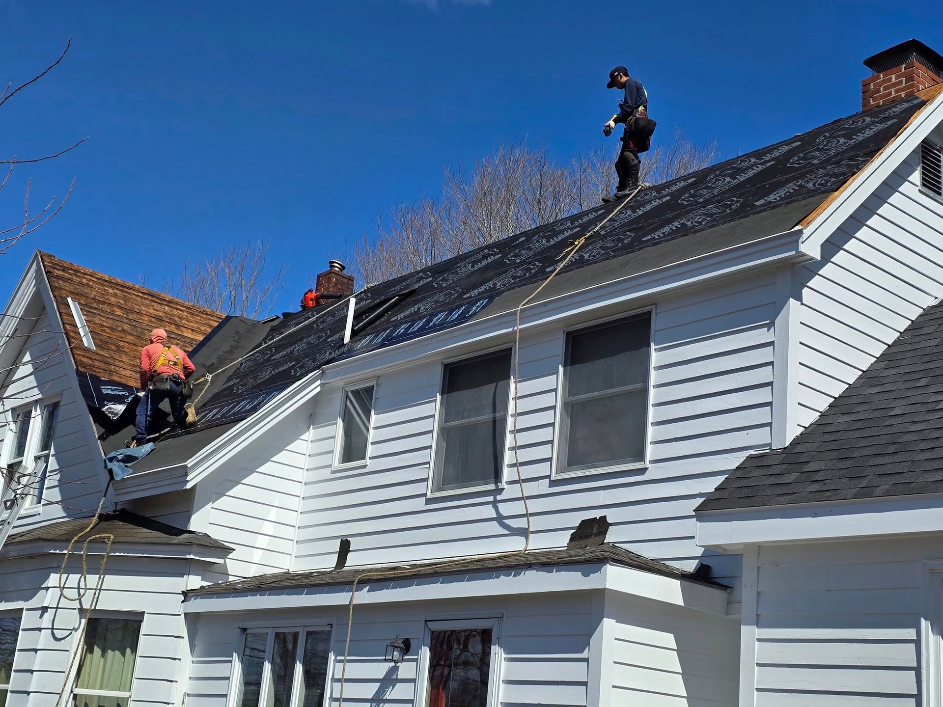 Workers on a white house roof repairing shingles on a sunny day