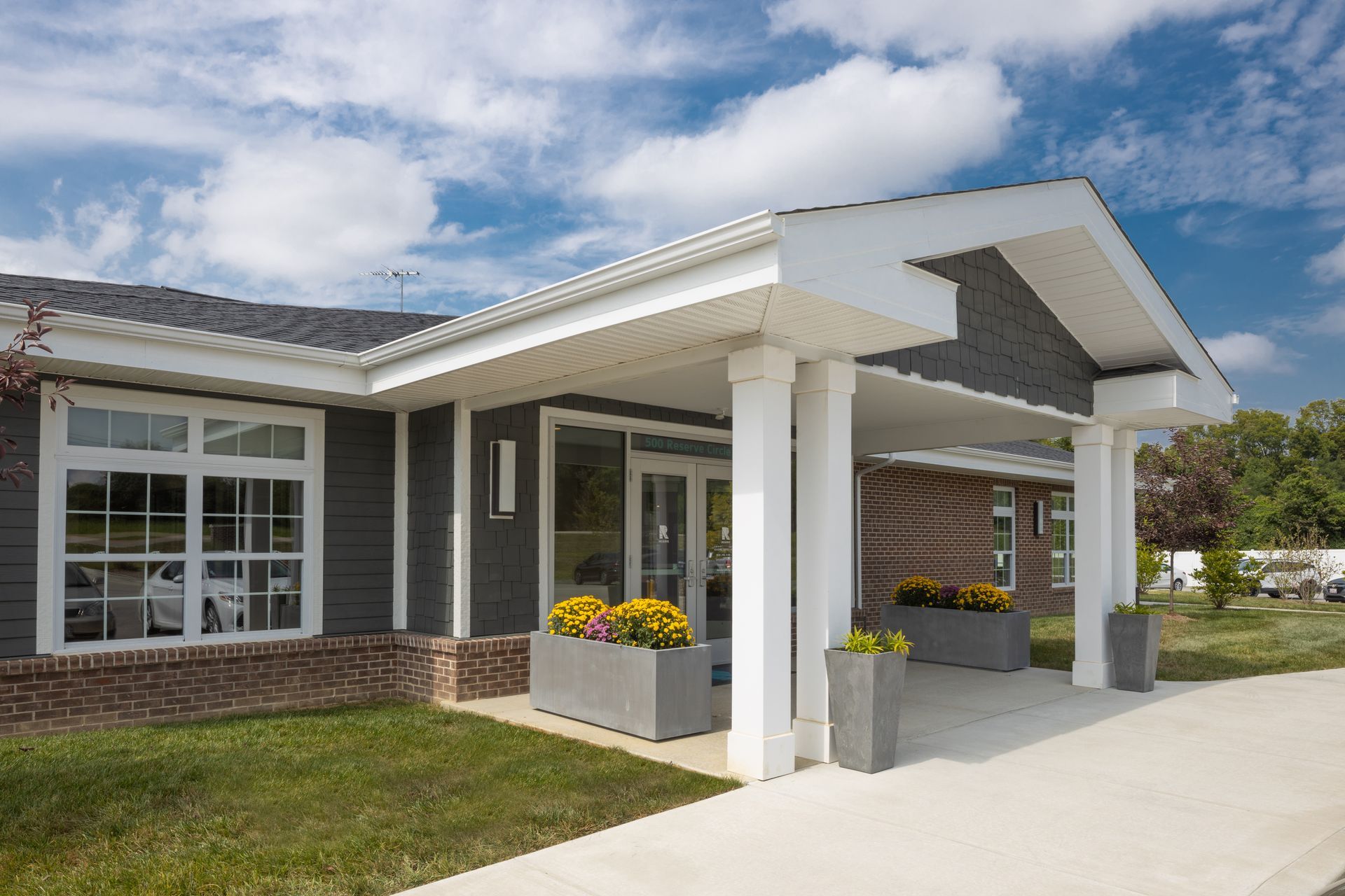 Building exterior with covered entrance, white columns, grey siding, and flower boxes.