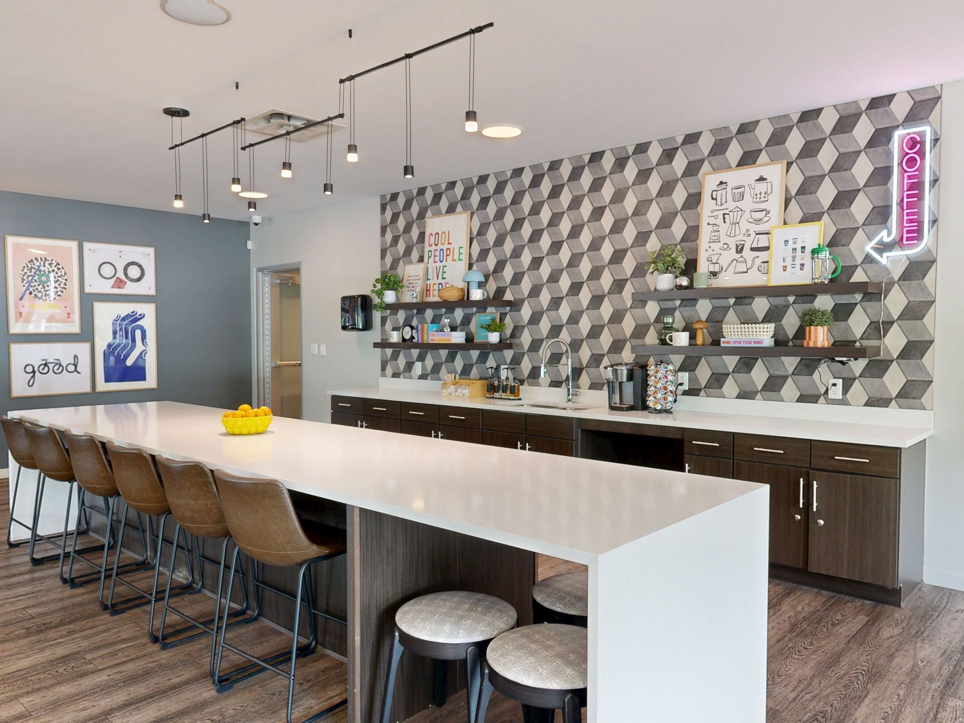 Modern lounge with multiple couches, TV, chairs, and tables. Light gray walls, wood floors.