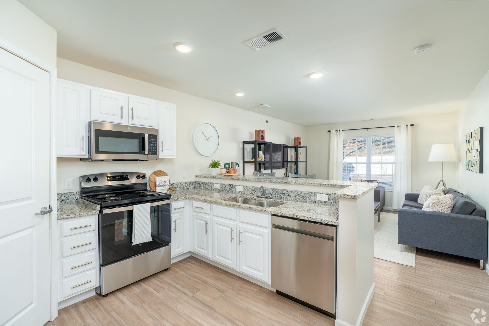 Modern kitchen with stainless steel appliances, white cabinets, granite countertops, and a view into a living area.