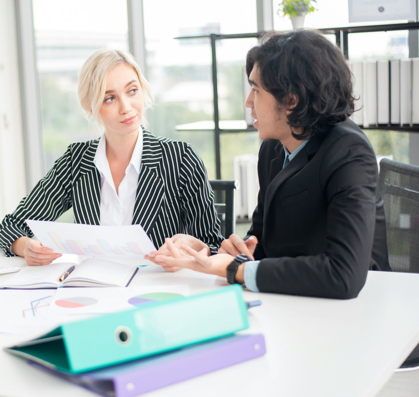 Woman and man reviewing documents at a wooden table in an office setting.