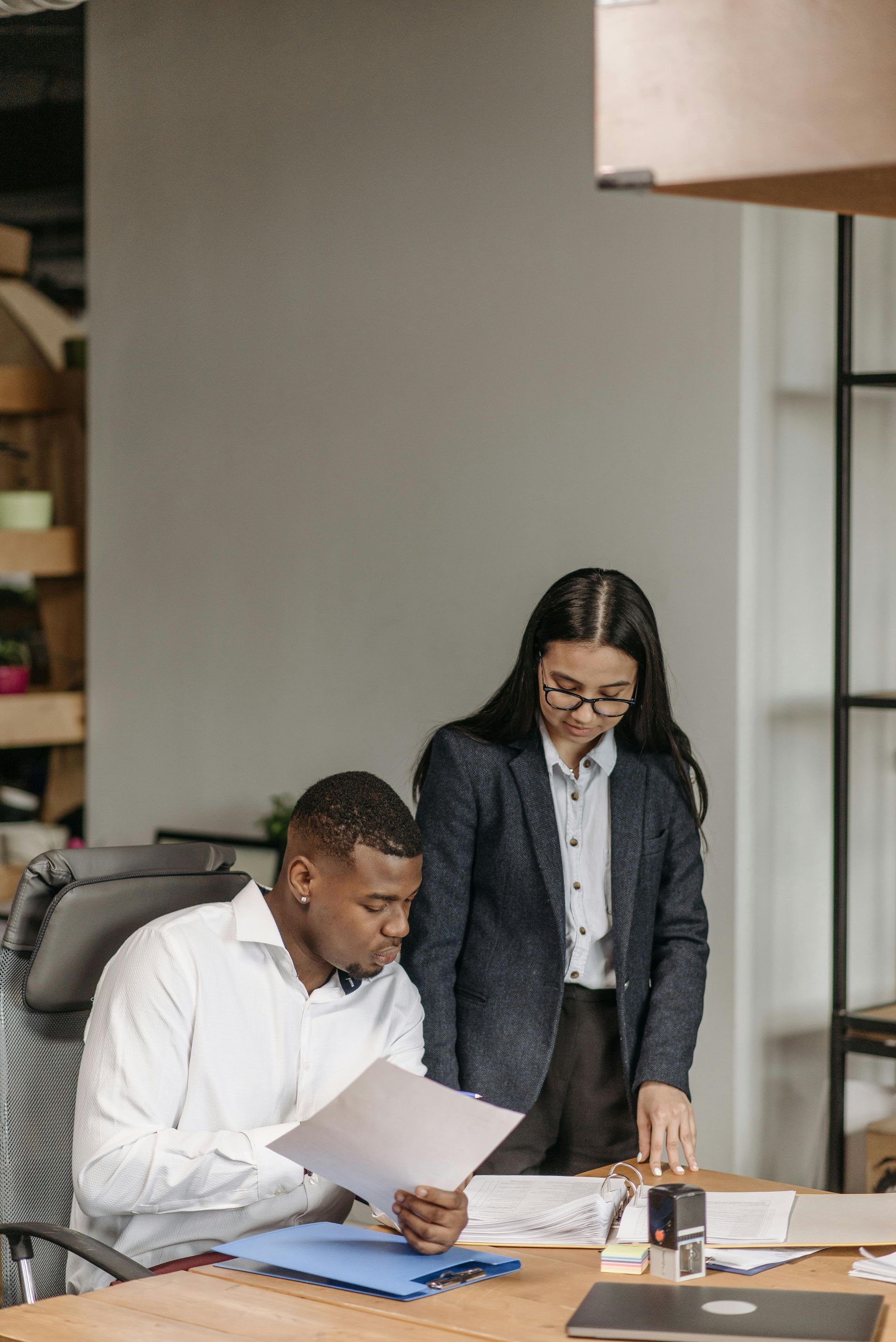 Woman and man reviewing documents at a wooden table in an office setting.