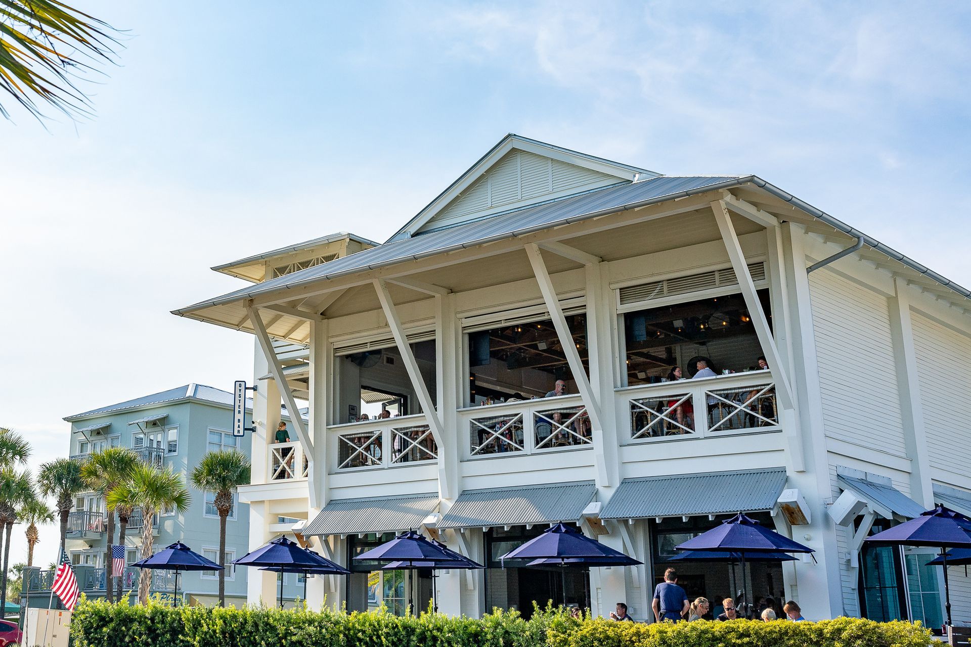 White coastal building with blue umbrellas and palm trees by the water