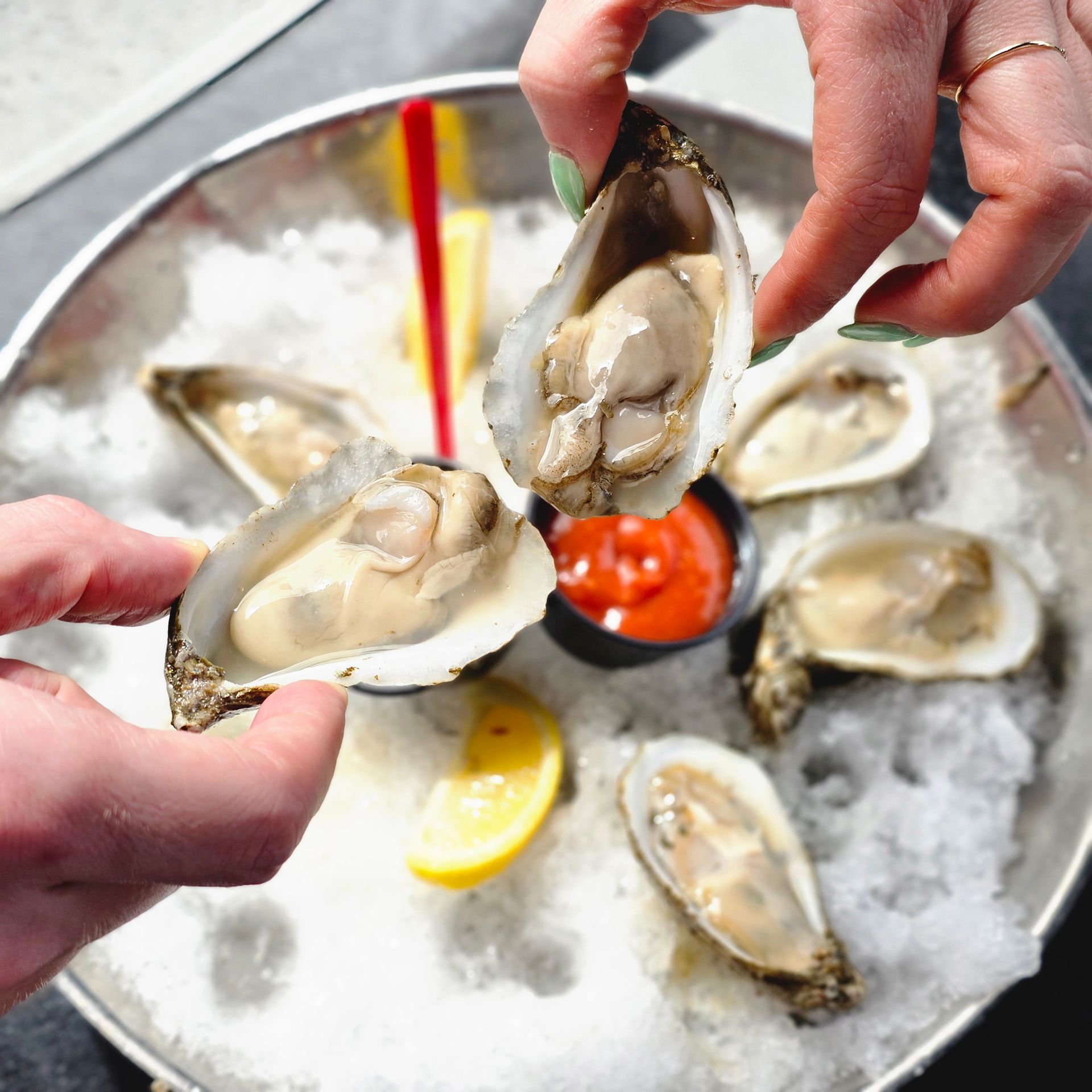 Hands holding open raw oysters on ice with lemon wedges and cocktail sauce