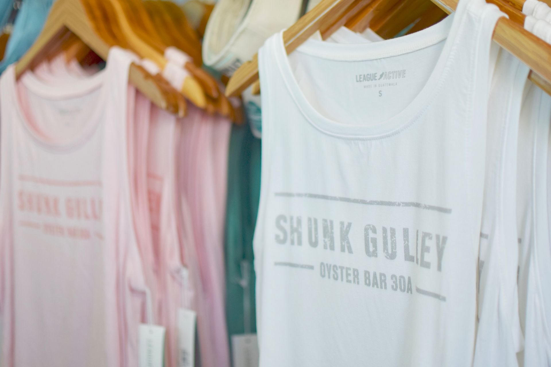 Pastel tank tops on hangers, including a white shirt with “SKUNK GULEY” text.