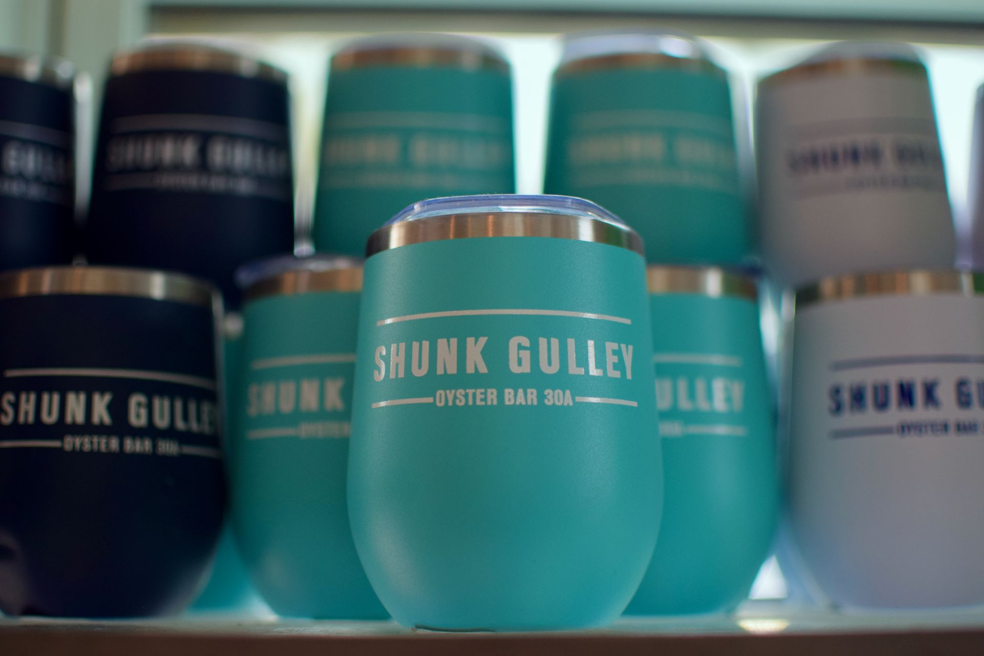 Stacked Skunk Gulley oyster stout cans in teal, black, and white on a shelf.