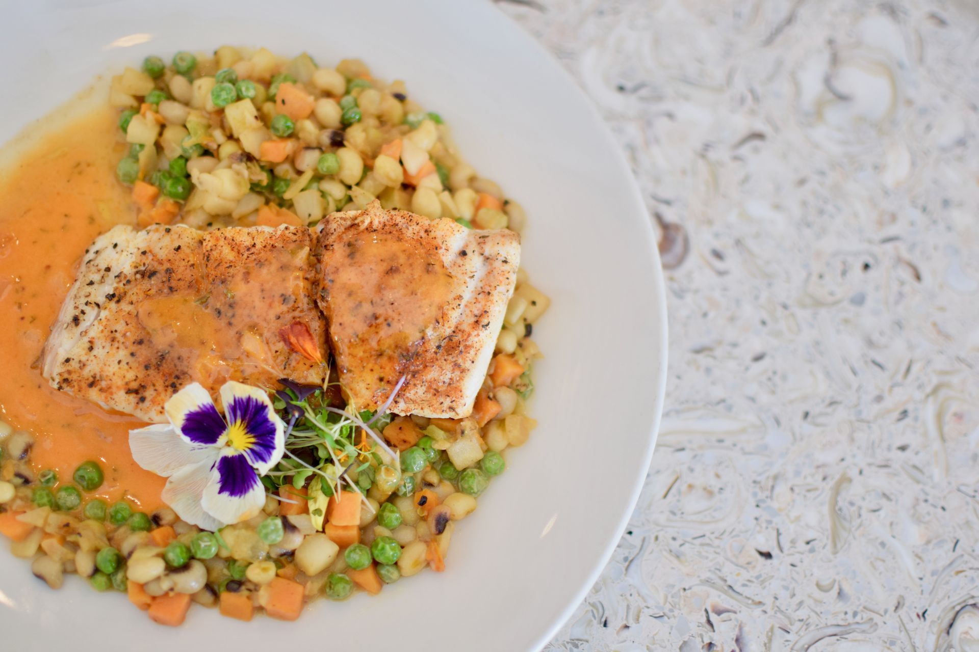 Seared salmon over vegetable couscous, garnished with edible flowers on a white plate