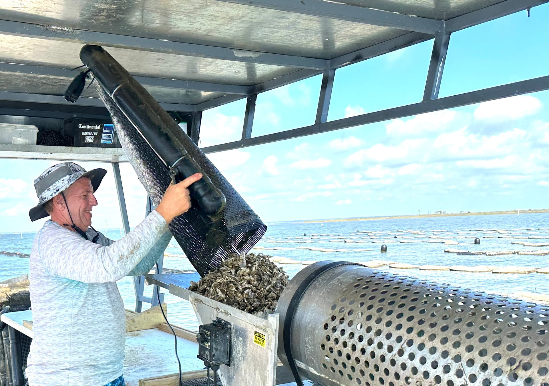 Worker pours seaweed into a sorting machine on a boat deck by the ocean.