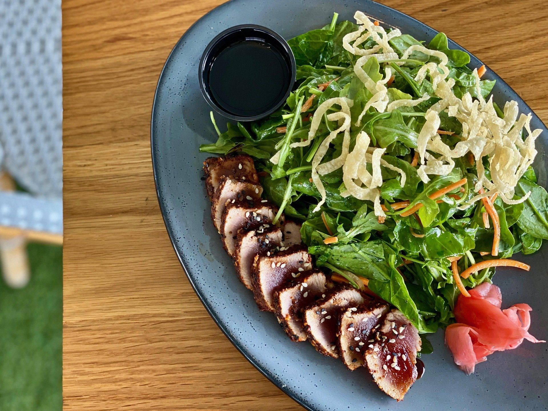 Sliced glazed meat with salad and pink pickled ginger on a blue plate with dipping sauce