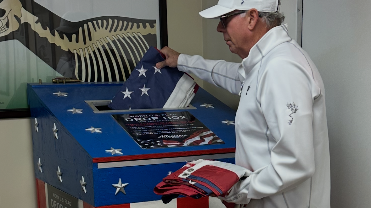 Man placing a folded American flag on a blue memorial box decorated with stars and stripes