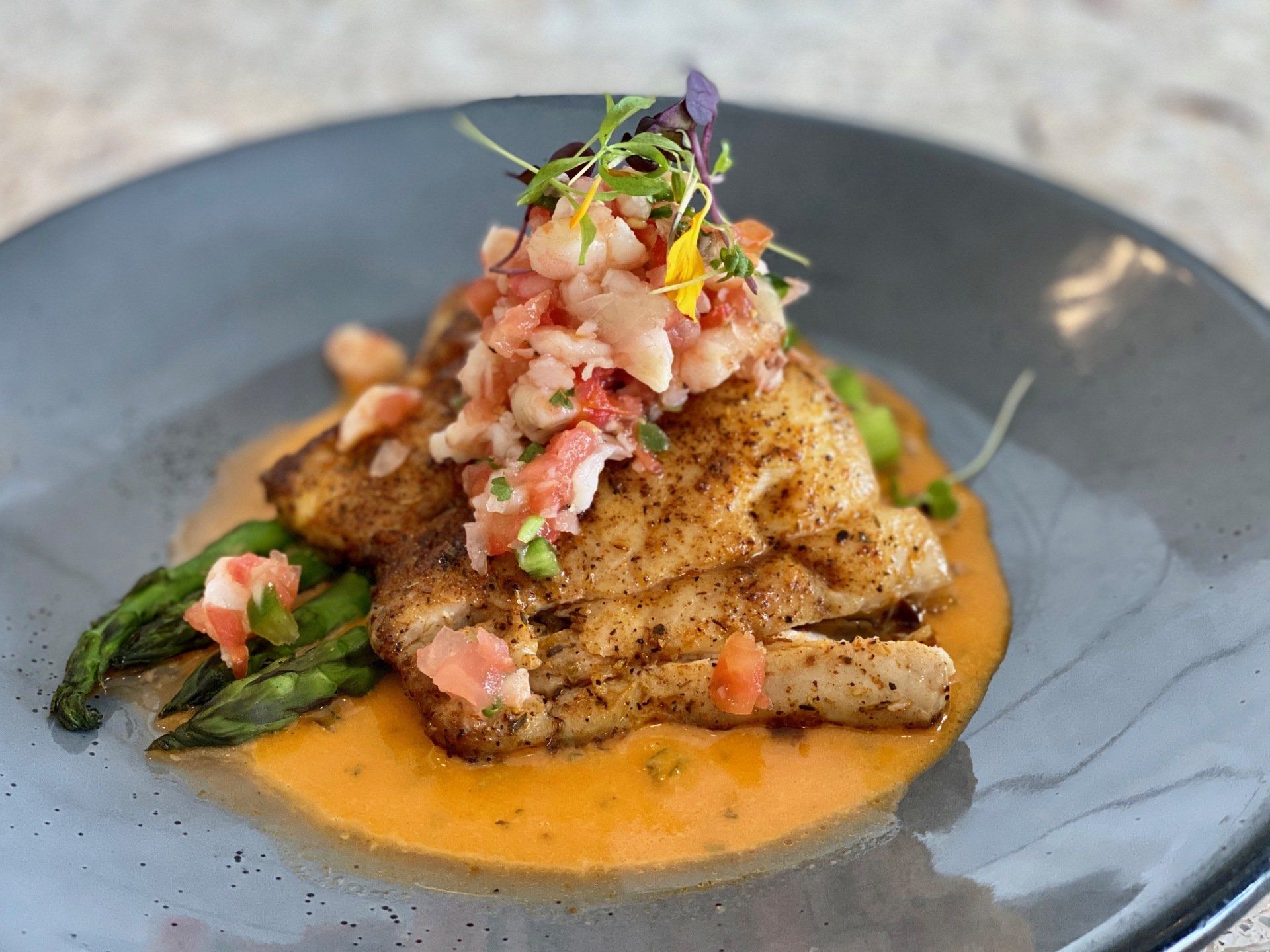 Grilled fish fillet with creamy orange sauce, topped with salsa, served on a gray plate with greens