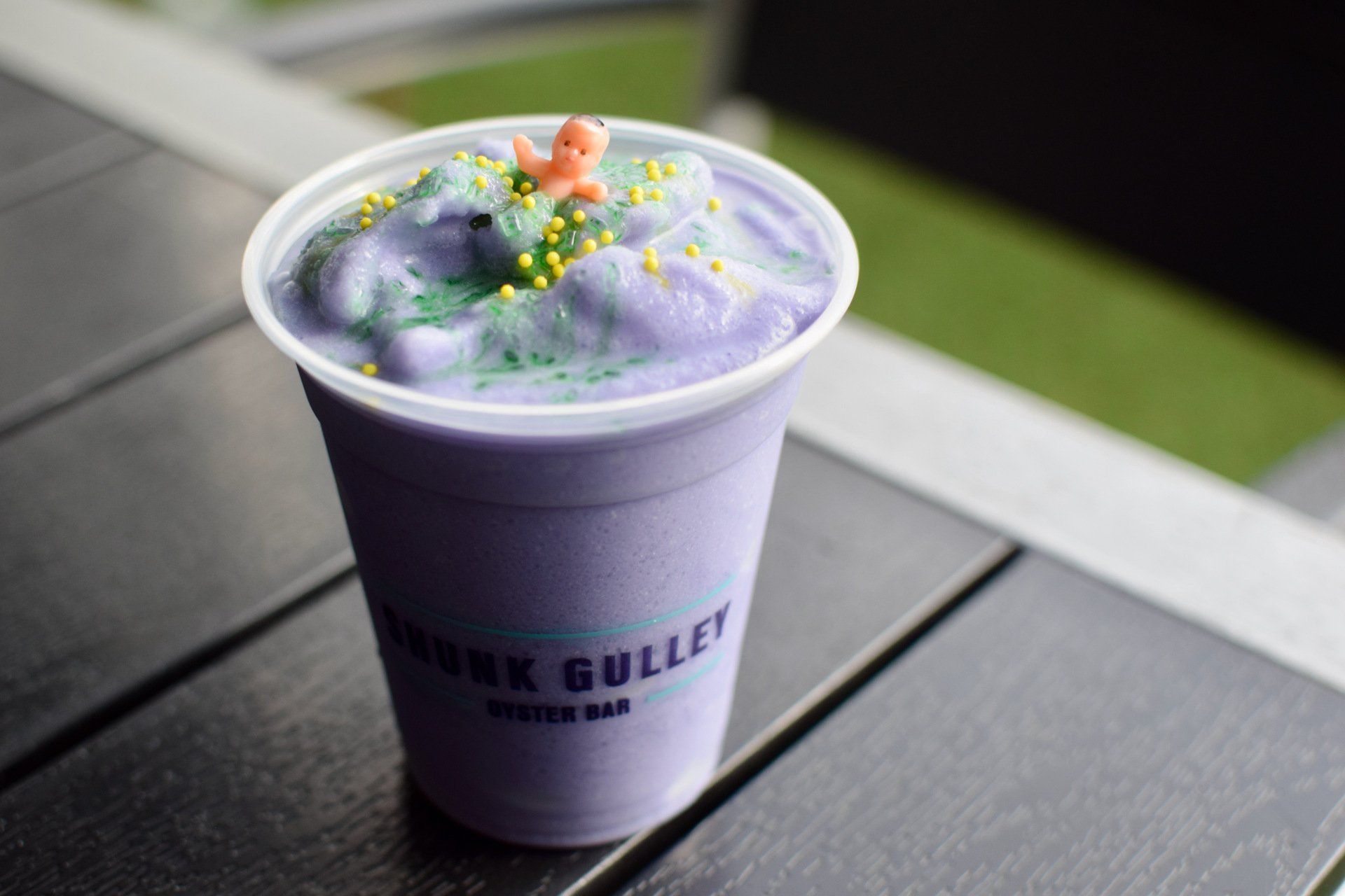 Purple smoothie in a cup on a dark table, topped with foam, berries, and flower petals.