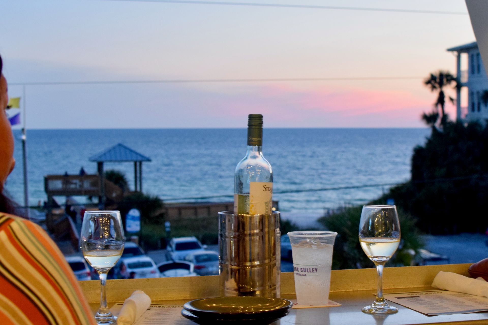 Table with wine glasses and a bottle overlooking the ocean at sunset