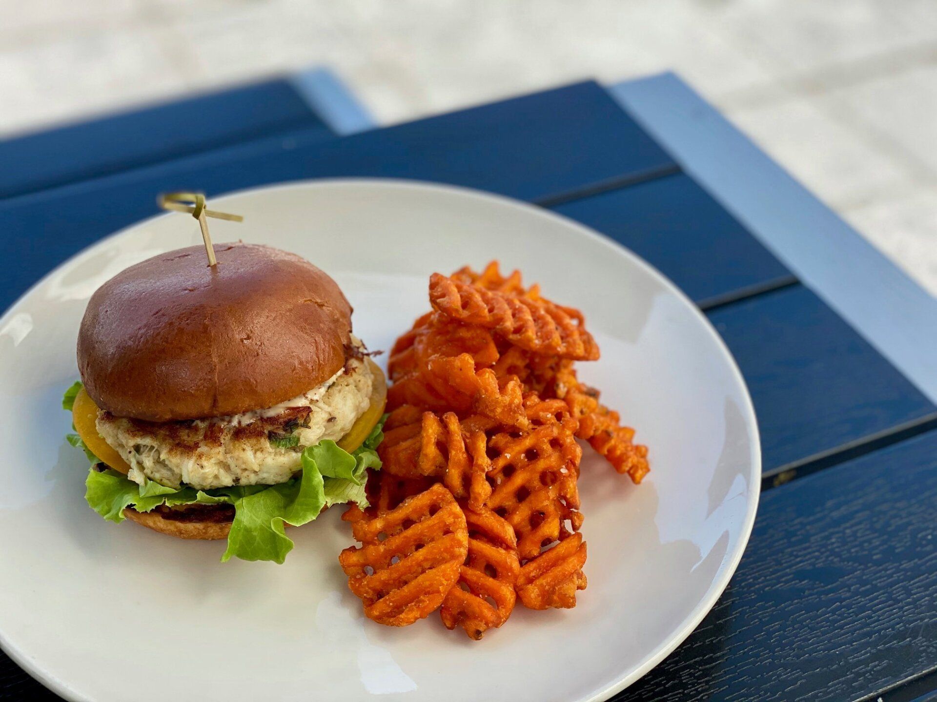 Burger and crinkle-cut fries on a white plate on a blue table