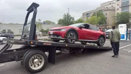 Red sports car being loaded onto a tow truck in a parking lot, with a man standing beside it.