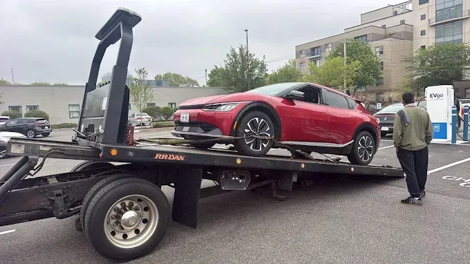 Red sports coupe on a tow truck with a man standing beside it in a parking lot.