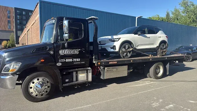 Black flatbed tow truck carrying a white SUV in a parking lot