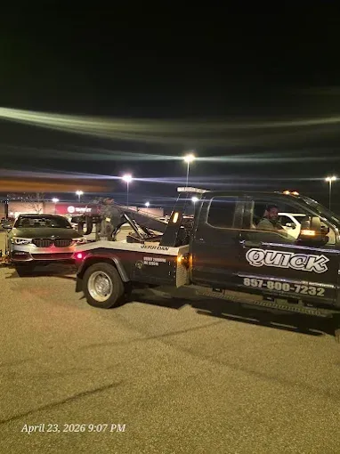 Tow truck hauling a black car at night in a parking lot