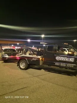 Tow truck hauling a damaged black car at night in a parking lot