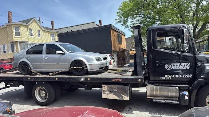 Tow truck hauling a silver sedan on a flatbed in a residential street.