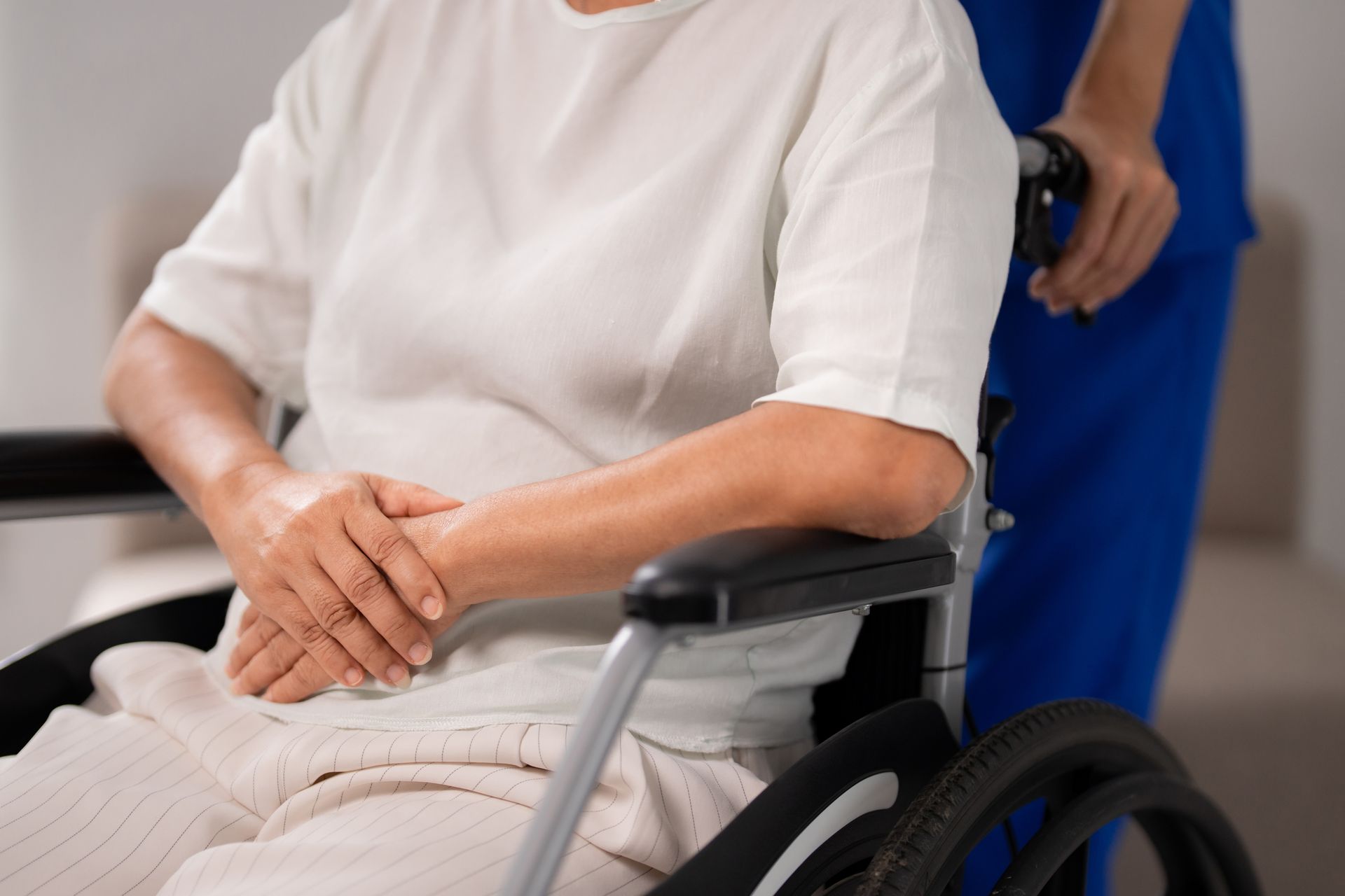 Smiling caregiver attends to senior woman resting on a pillow indoors. Senior woman in a wheelchair with a caregiver at an assisted living facility