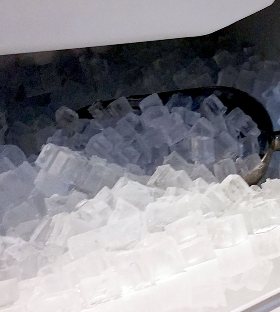 A close-up view of a metal scoop inside a bin filled with clear, cube-shaped ice.