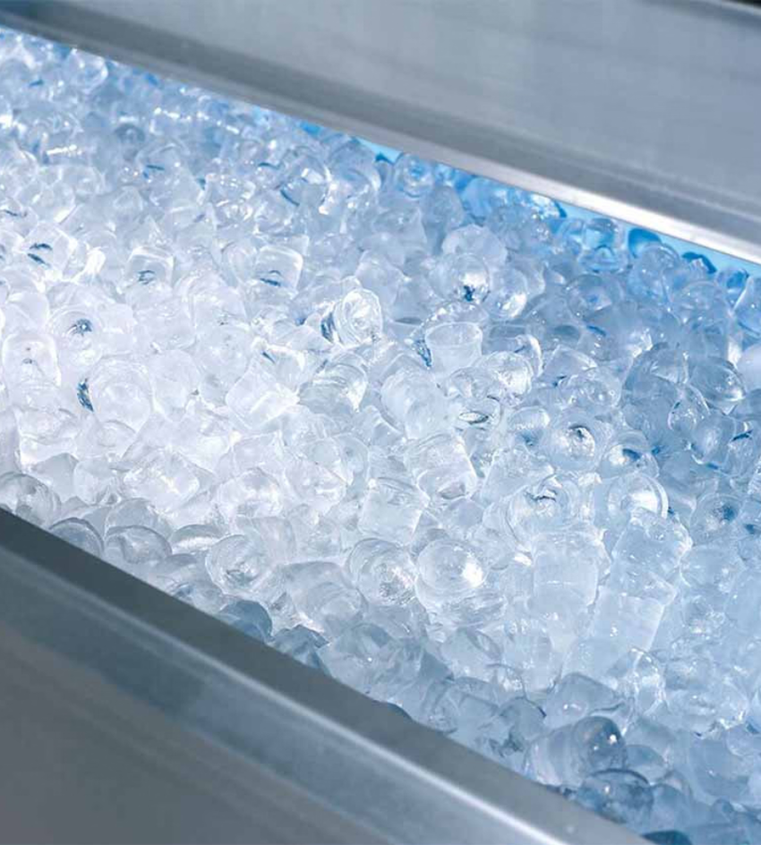 A close-up, high-angle shot of a metal bin filled with clear, faceted ice cubes lit with a cool blue hue.