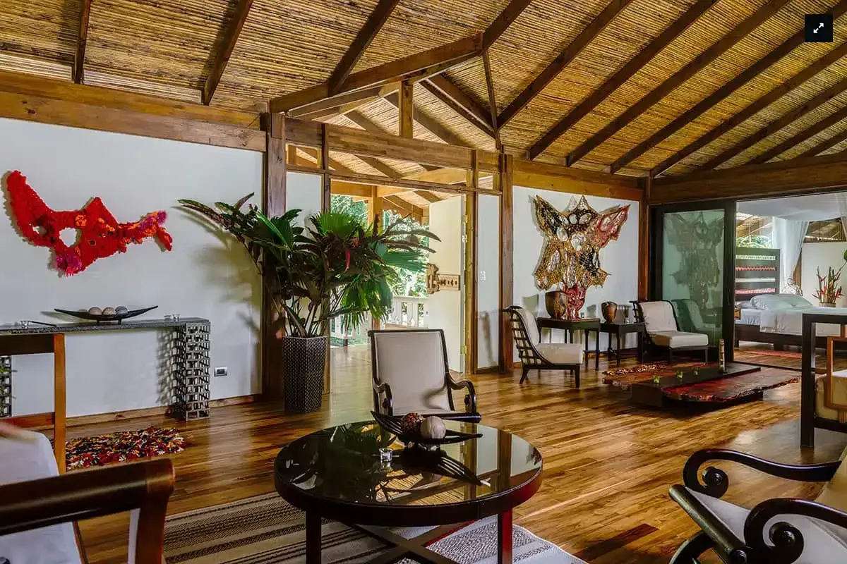 Wooden lodge-style living room with woven ceiling, abstract wall art, plants, and seating around glass tables Pacuare Lodge, Pacuare River