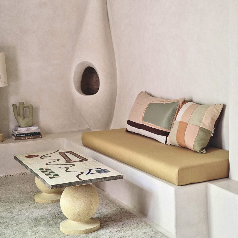 A minimalist lounge area with a built-in white bench, mustard cushion, patterned pillows, and a sculptural coffee table.