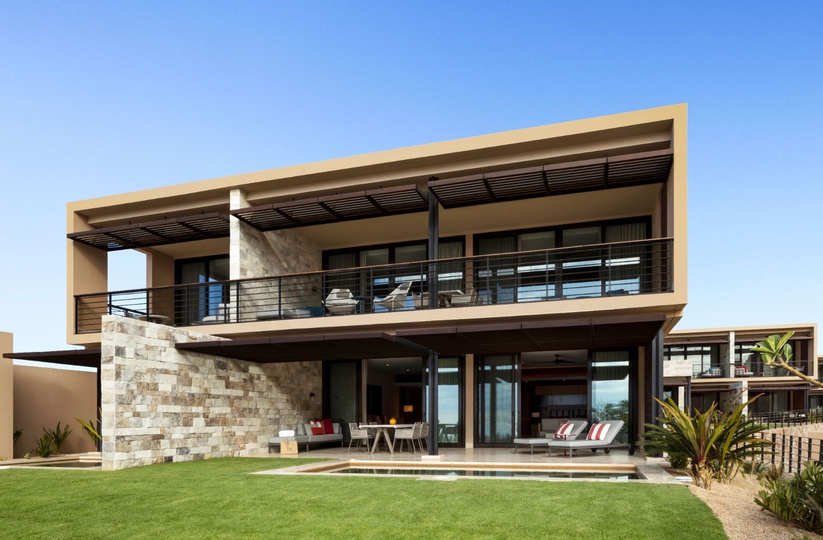 Modern two-story home with stone accents, glass balcony, and a green lawn under a clear blue sky Montage Los Cabos
