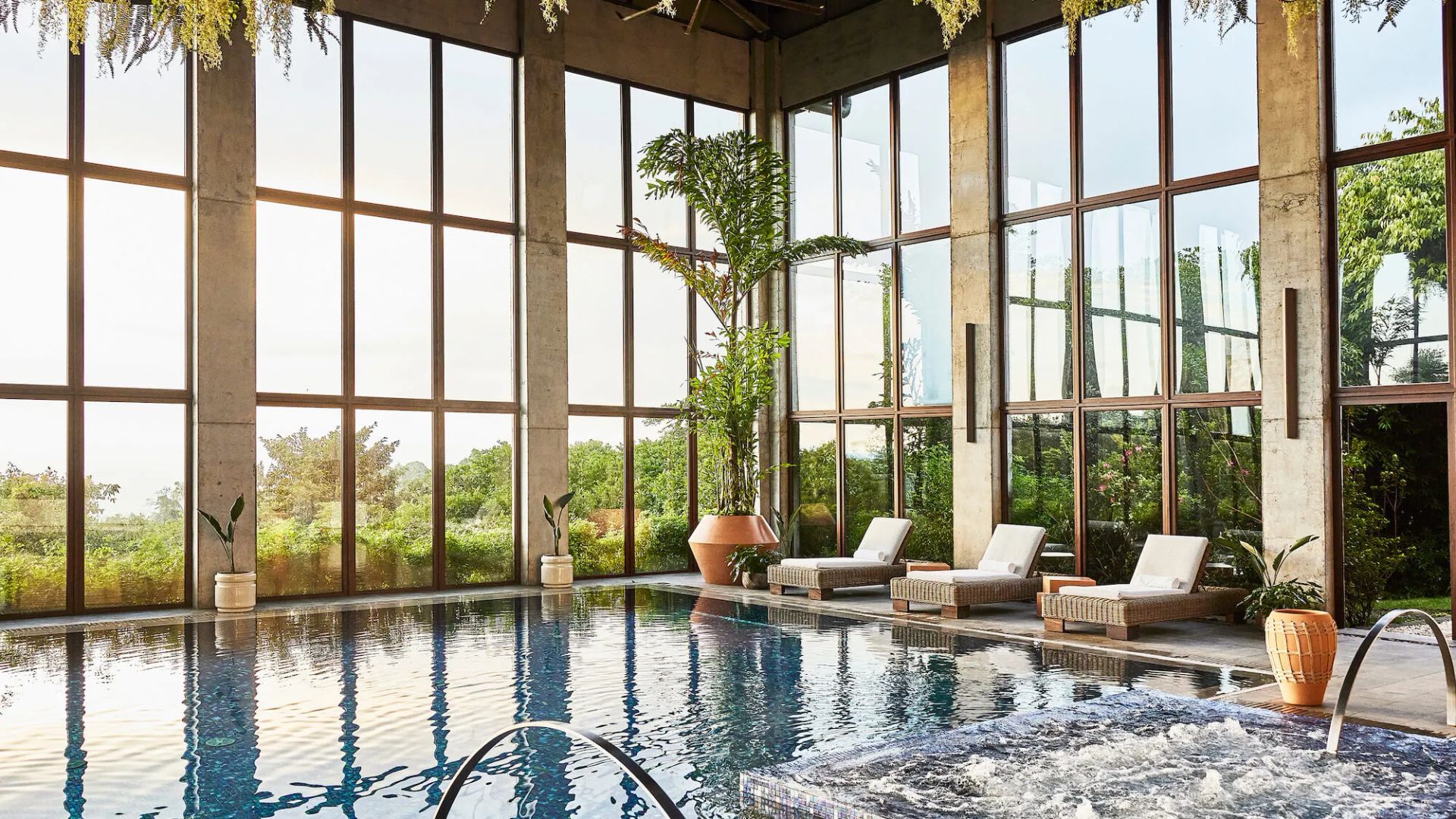 Bright indoor pool with lounge chairs and floor-to-ceiling windows overlooking lush greenery Hacienda AltaGracia, Auberge Resorts Collection