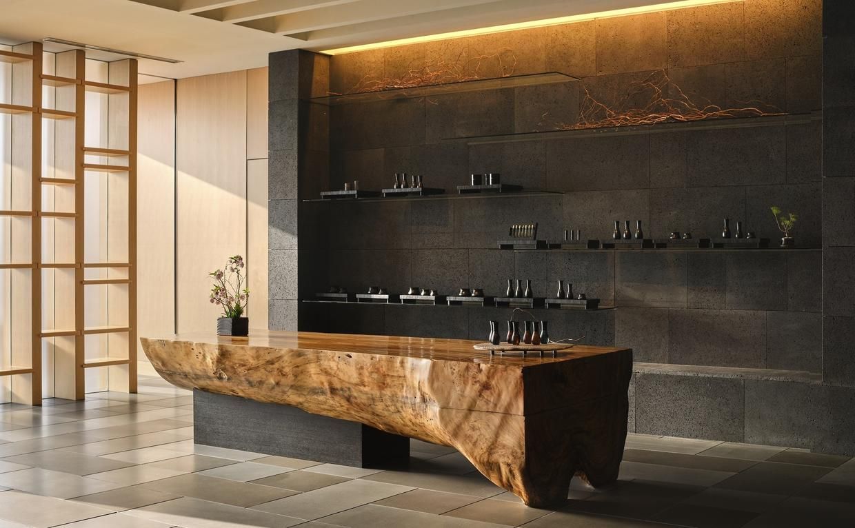 Reception area with a large wooden counter, gray stone wall and shelves. Aman Tokyo 