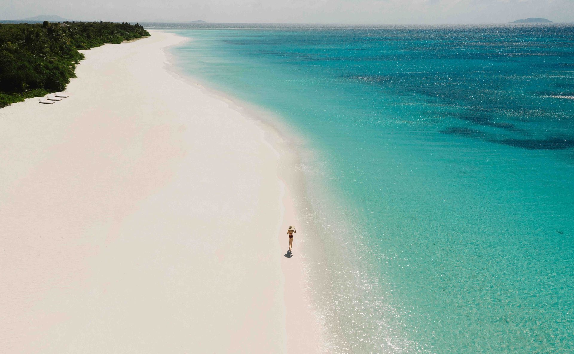 White sand beach meets turquoise ocean; person stands in shallows. Amanpulo, Philippines