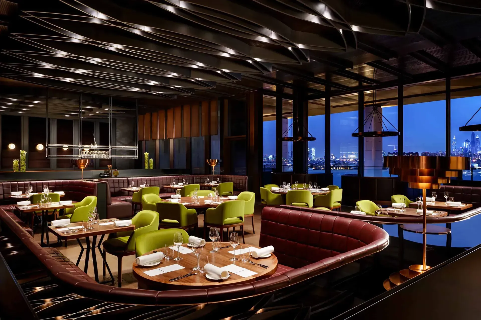Upscale restaurant interior with green chairs, booths, tables, and city skyline view. Atlantis The Royal