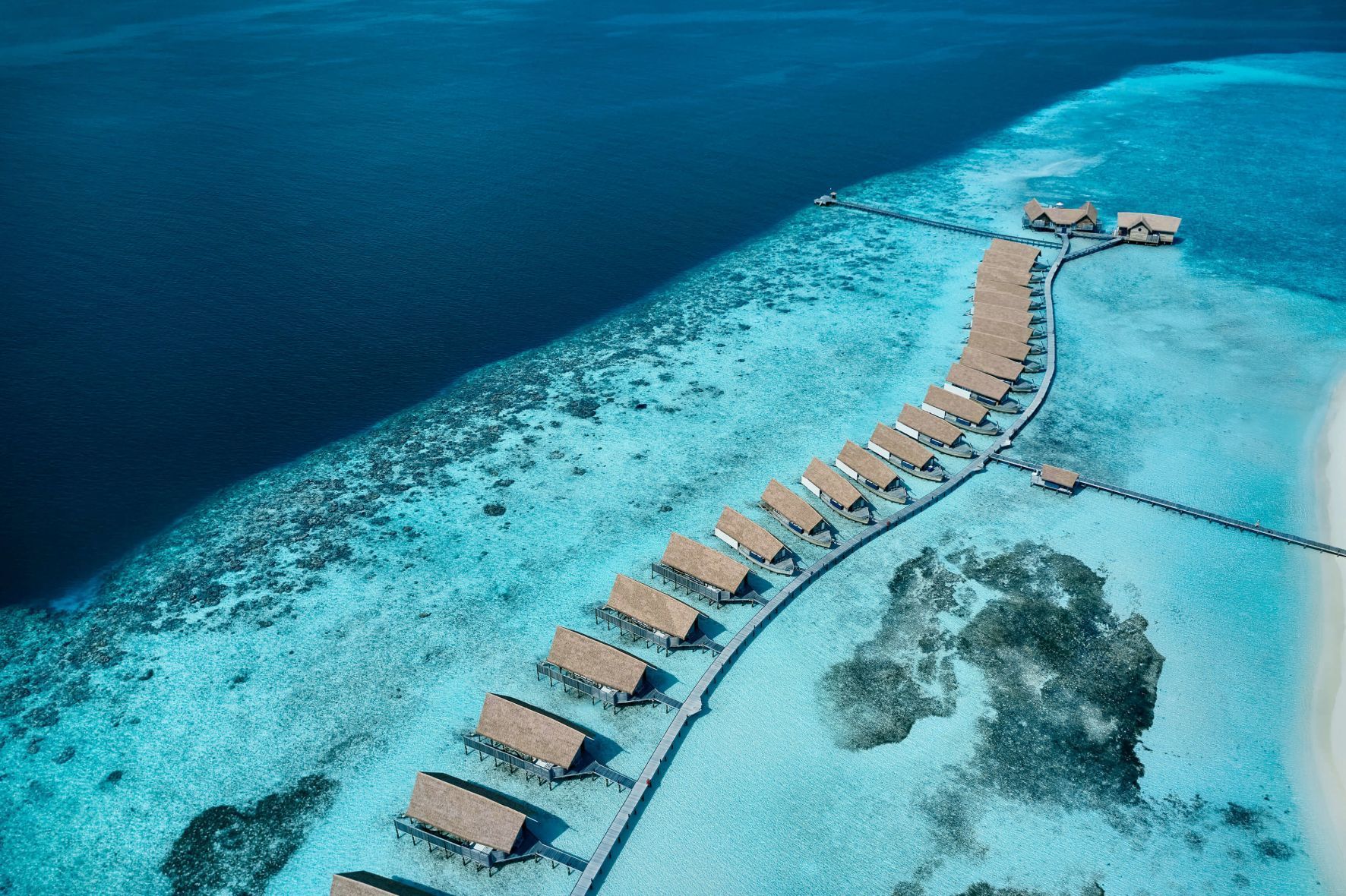 Overwater bungalows on a sandy strip of land in turquoise waters.