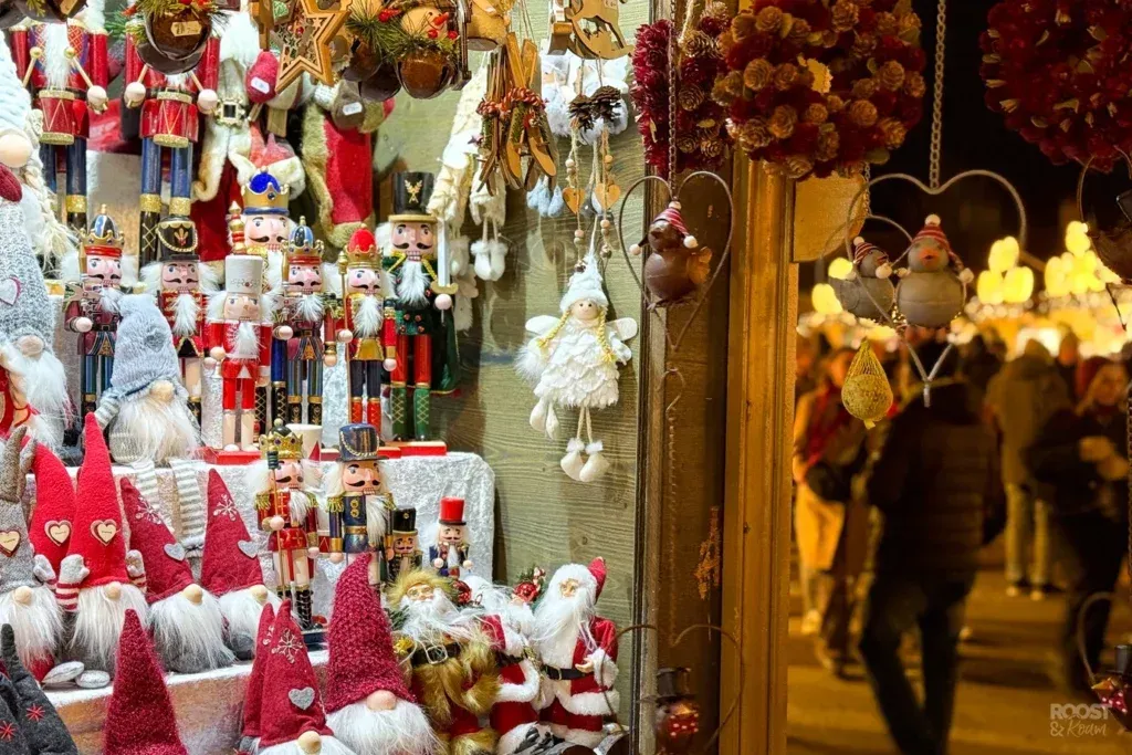 Christmas market stall with holiday decorations, including gnomes, nutcrackers, and Santa figures. A blurred crowd is visible.