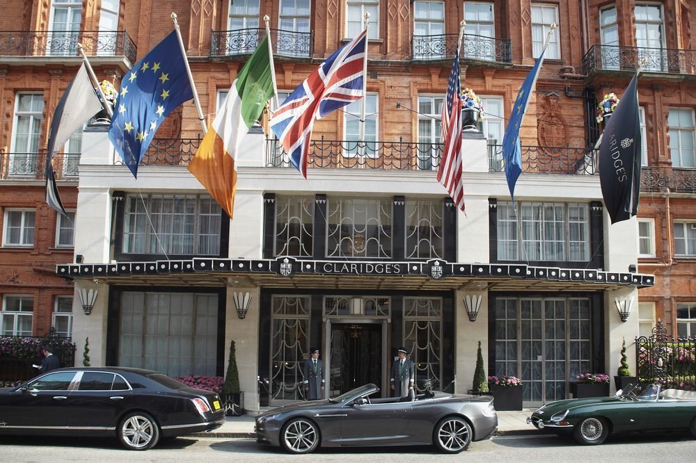Exterior of a red brick building with flags, including EU, Irish, and British. Cars parked in front.