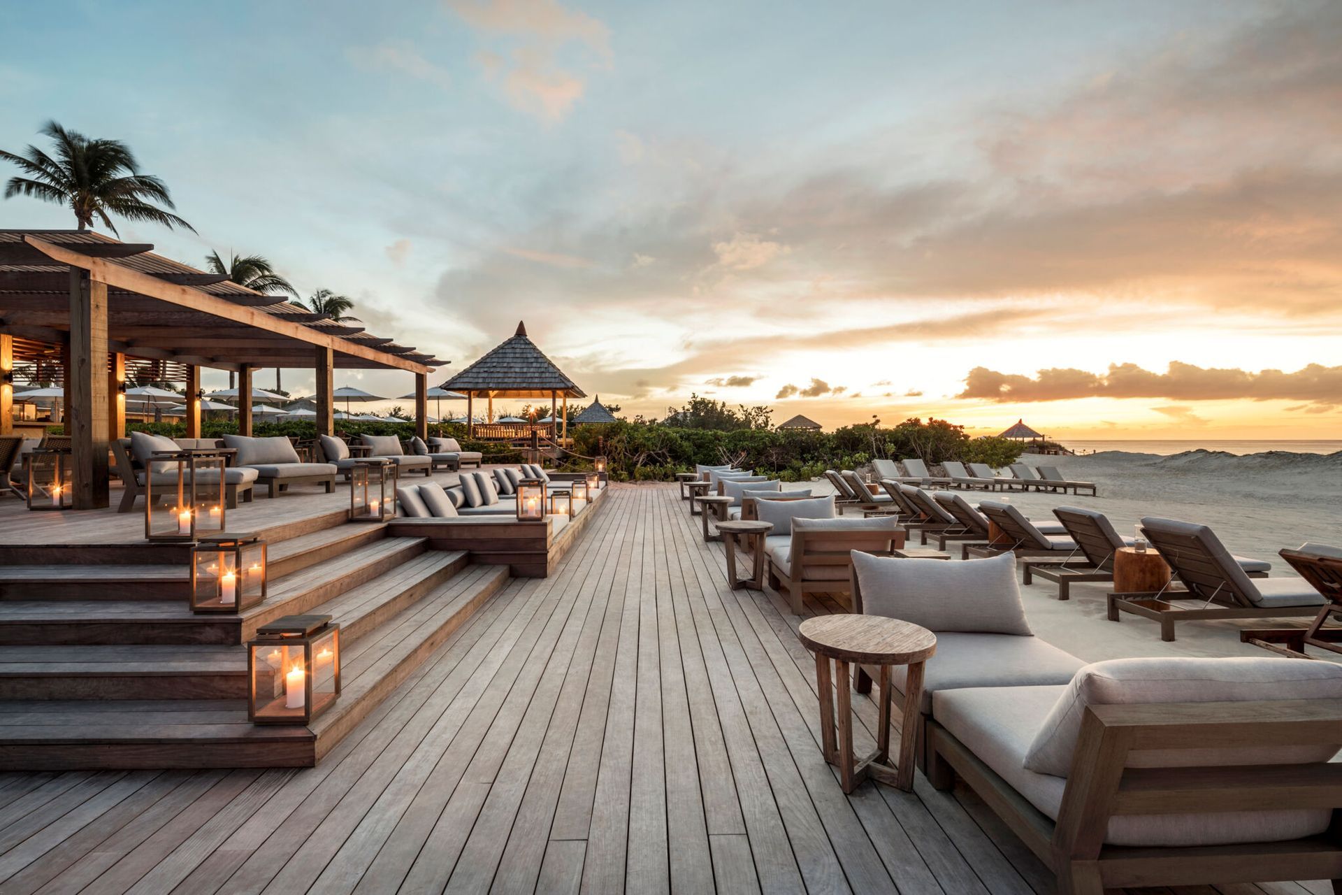 Wooden deck with lounge chairs, steps, and a gazebo overlooking a beach at sunset. Como Parrot Cay, Turks and Caicos